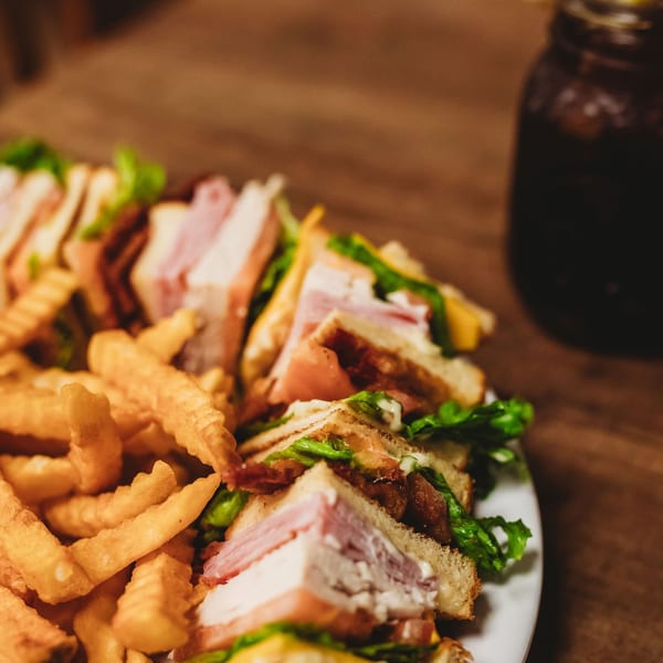 Club sandwiches with fries and a drink with a lemon wedge on a wooden table.
