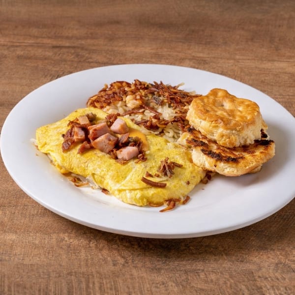 Breakfast plate with a ham and bacon omelet, hash browns, and a biscuit on a white plate.