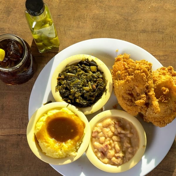 Southern comfort food plate with fried chicken, collard greens, mashed potatoes, beans, and iced tea.