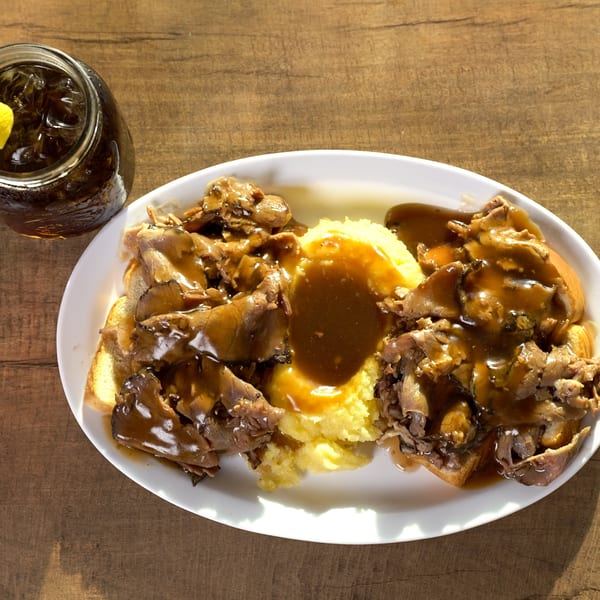 A hot beef sandwich with mashed potatoes and gravy, served with an iced tea.