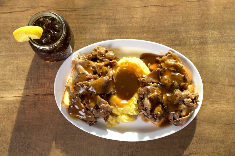A hot beef sandwich with mashed potatoes and gravy, served with an iced tea.