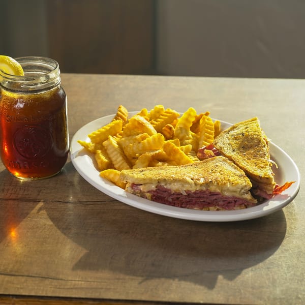 Reuben sandwich with crinkle-cut fries and iced tea with a lemon slice on a wooden table.
